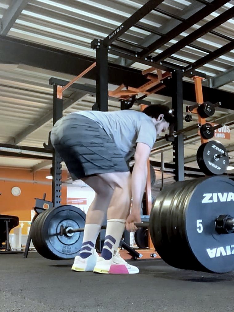 Sportif en position de départ d'un soulevé de terre, barre chargée, en salle de musculation